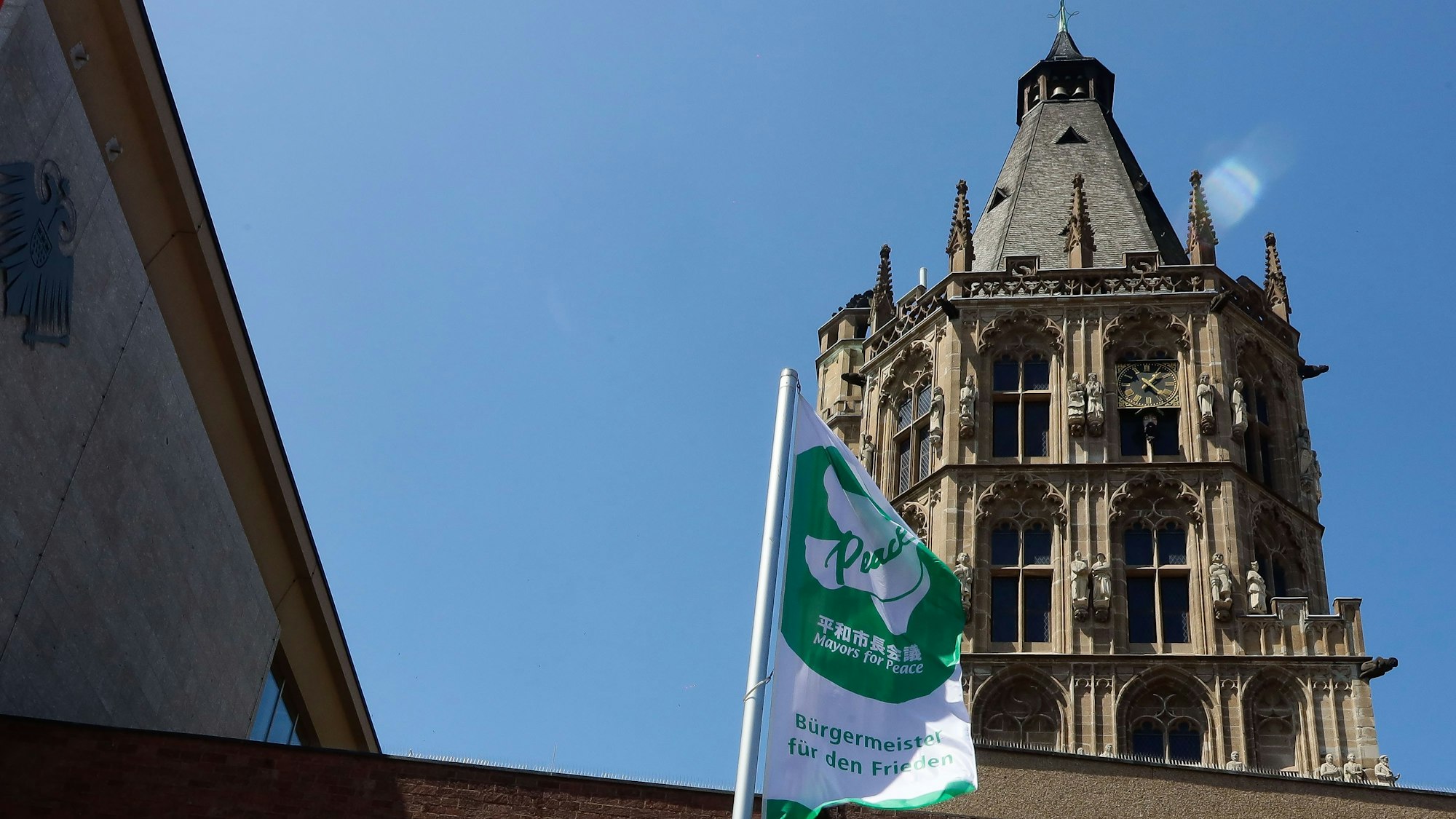 Das Bild zeigt die weiß-grüne Flagge von „Mayors For Peace“ vor dem Rathausgebäude. Im Hintergrund ist der Rathausturm zu sehen.
