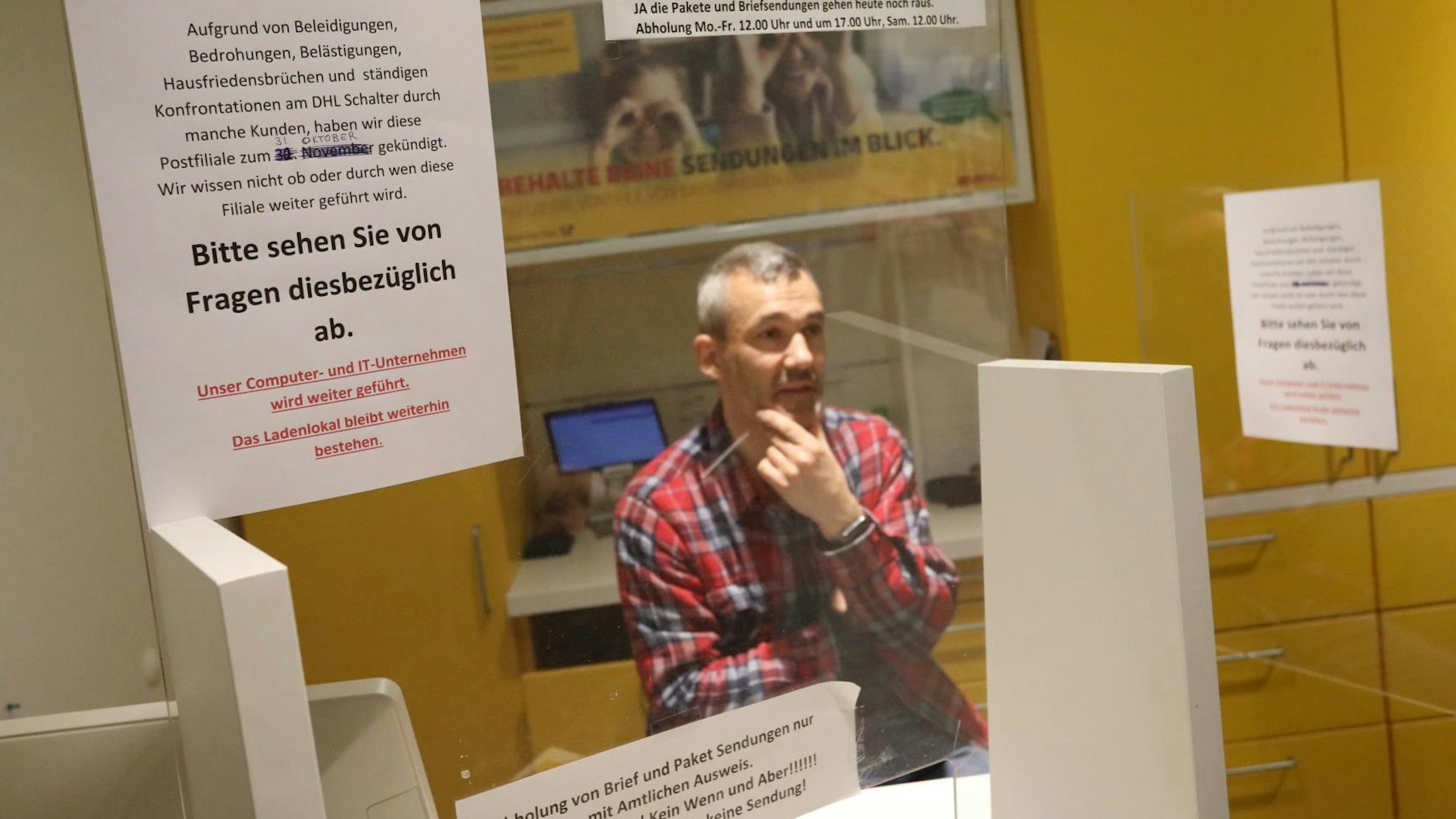 Ein Mann in kariertem Hemd sitzt hinter einem Schalter der Postfiliale in Königswinter.