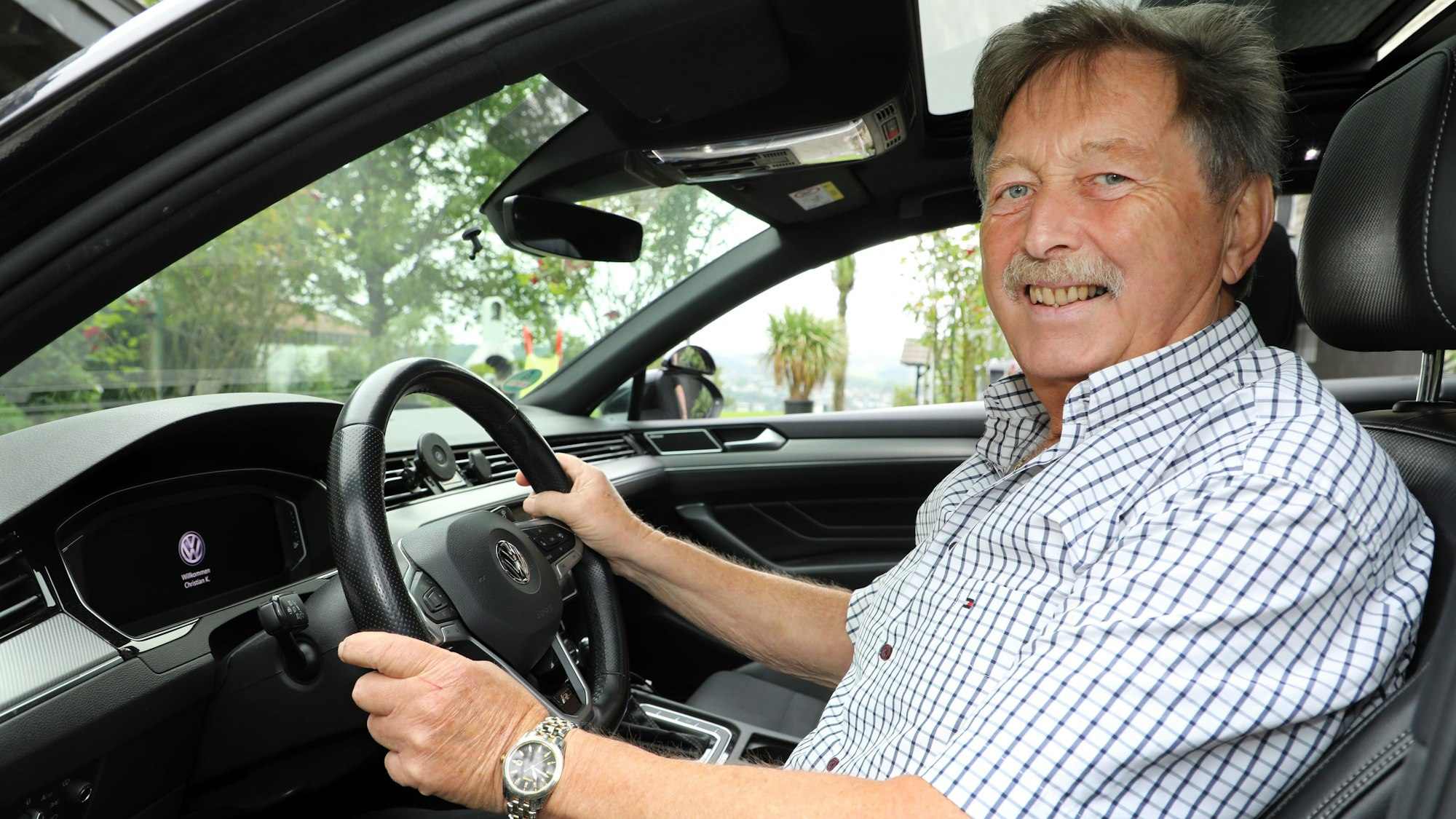 Ein Mann sitzt lächelnd am Lenkrad eines Wagens.