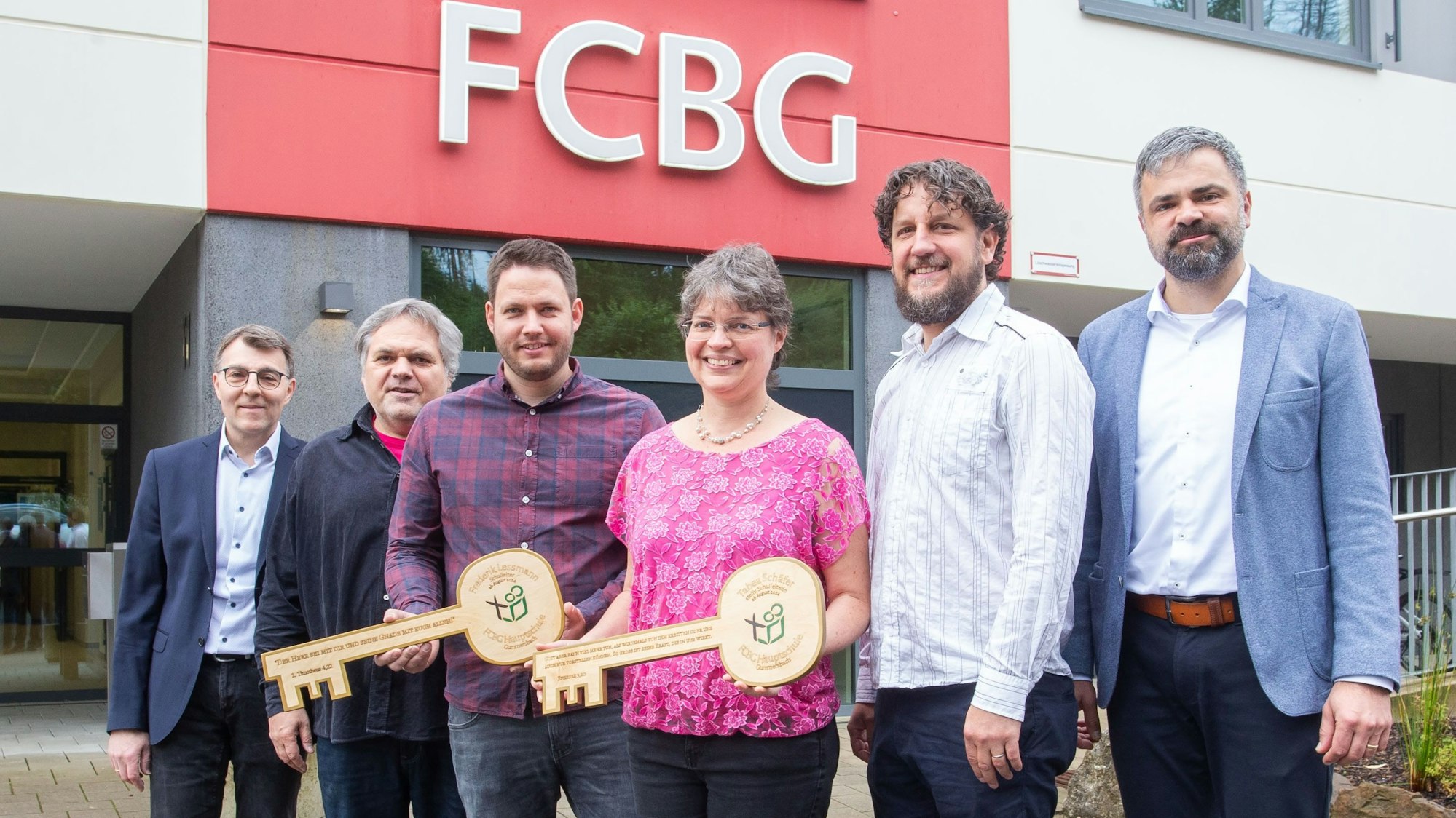 Schlüsselübergabe bei der FCBG-Hauptschule (v.l.): Jakob Holzrichter (Schulträger), Ex-Schulleiter Thomas Sieling, Jan-Frederik Lessmann (neuer Schulleiter), Tabea Schäfer (neue stellvertretende Schulleiterin), Ralf Sassenhausen (ehemaliger stellvertretender Schulleiter), Viktor Pritzkau (Schulträger) stehen nebeneinander. Sie halten zwei große Schlüssel in den Händen.
