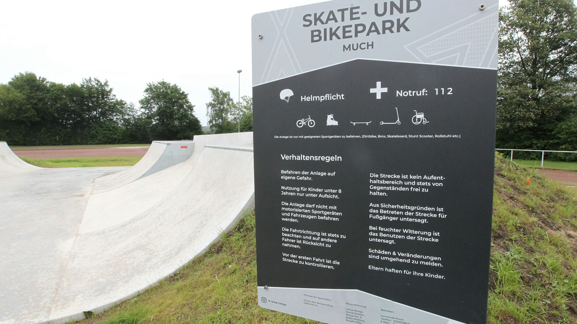 Ein Schild mit der Benutzungsordnung für den Skate- und Bikepark Much. Links ist ein Teil der Anlage zu sehen.