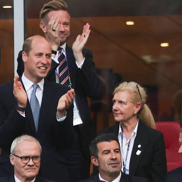 Prinz William klatscht grinsend in die Hände während er auf einer Tribüne steht.