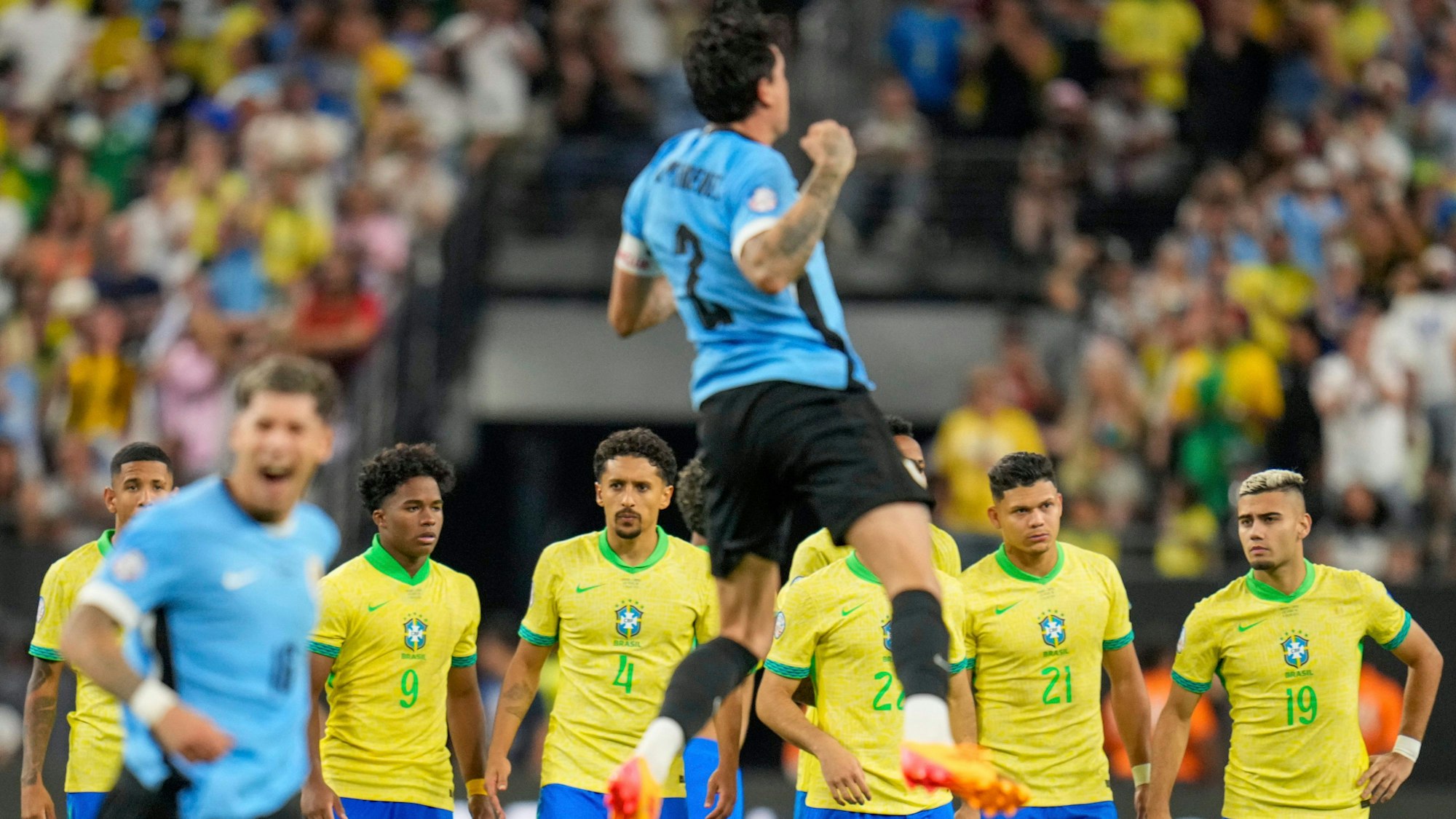 Brasilianische Spieler stehen im Mittelfeld, während uruguayische Spieler ihren Sieg im Elfmeterschießen während des Viertelfinales der Copa America feiern.