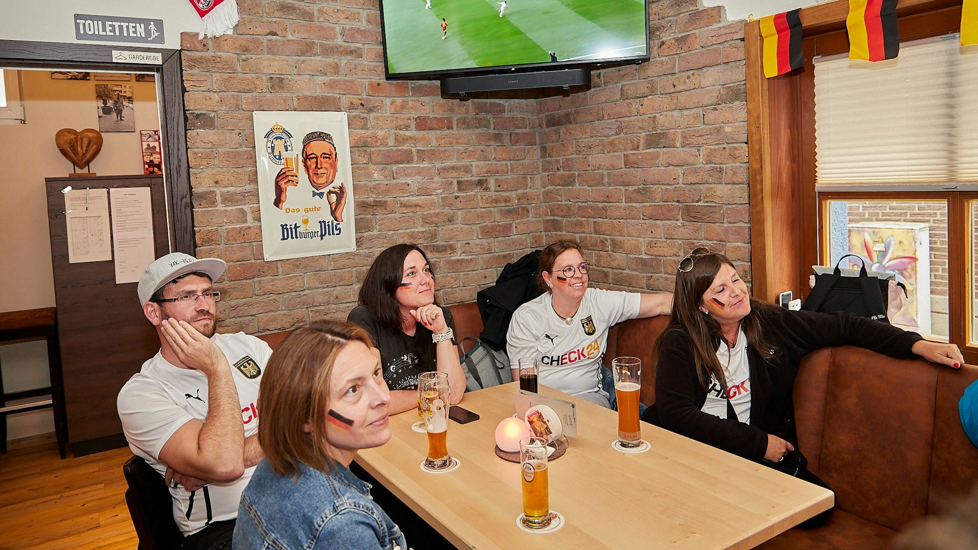 Das Bild fünf Deutschlandfans im Saal Gier, wie sie das Spiel auf einem Fernseher verfolgen.
