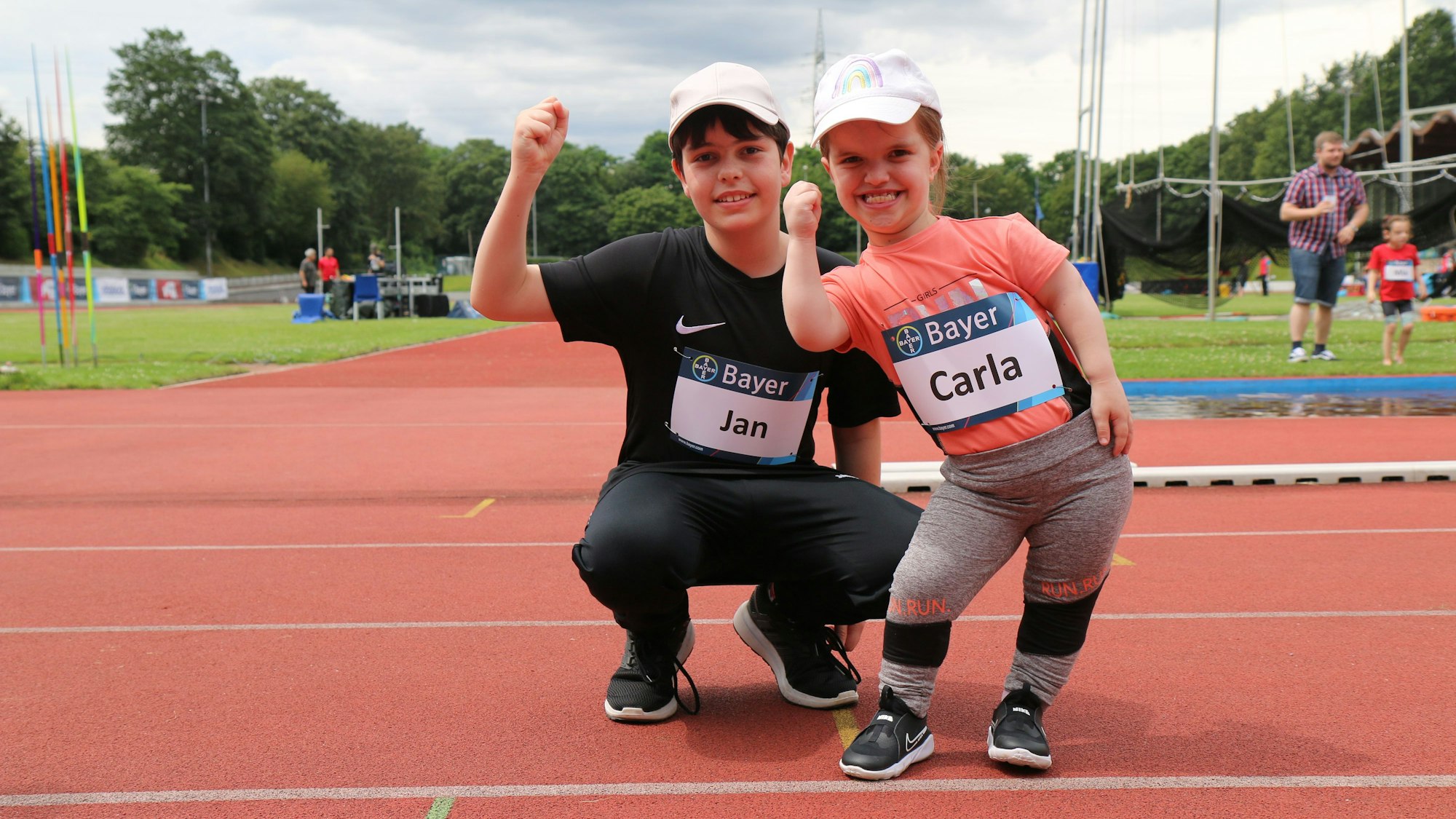 Die Geschwister Jan und Carla auf der Tartanbahn des Manforter Stadions. Sie lächeln in die Kamera und recken die Faust in die Höhe.