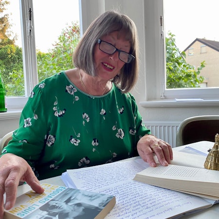 Heidrun Brenig sitzt an einem Tisch und liest in einem Buch.