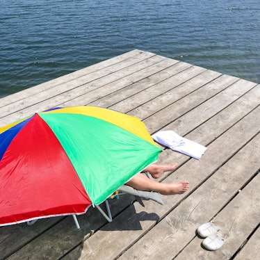 Das Bild zeigt eine Person, die fast komplett unter einem Sonnenschirm liegt, um sich vor den Sonnenstrahlen zu schützen.