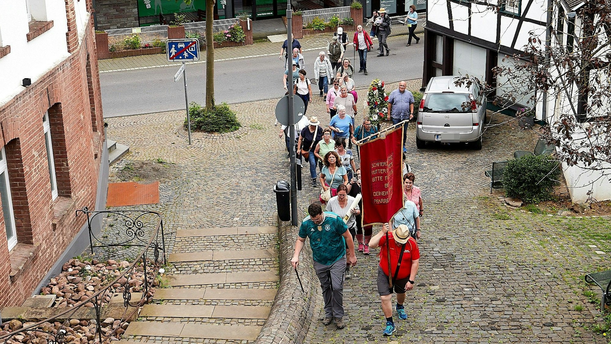 Eine Pilgergruppe geht einen gepflasterten Weg zur Kirche in Heimbach hinauf.
