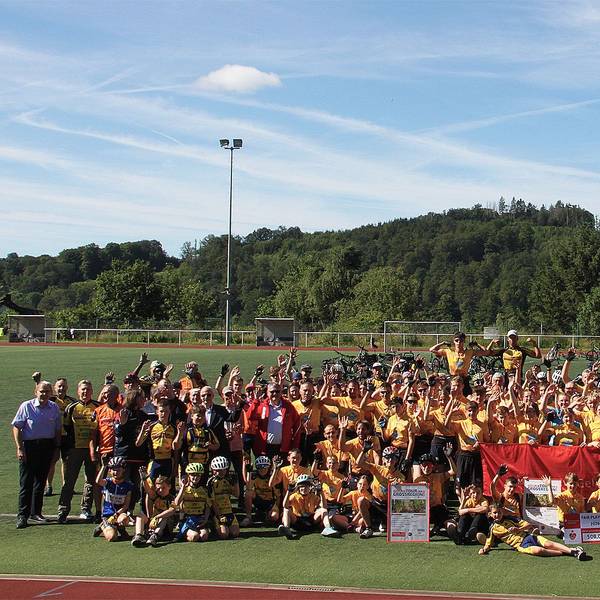 Viele Kinder, Jugendliche und Erwachsene haben sich zum Gruppenbild auf dem Sportplatz versammelt.