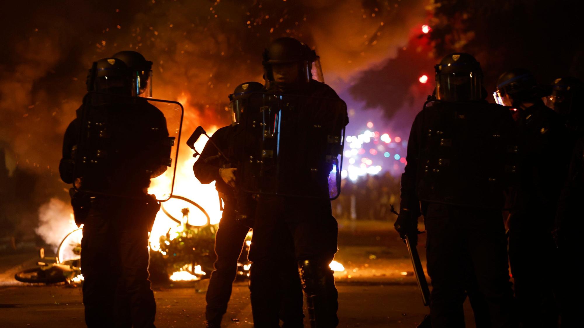 Frankreich, Paris: Polizisten stehen bei brennenden Fahrrädern während der Spannungen in der Nähe des Platzes der Republik nach der zweiten Runde der Parlamentswahlen in Paris.