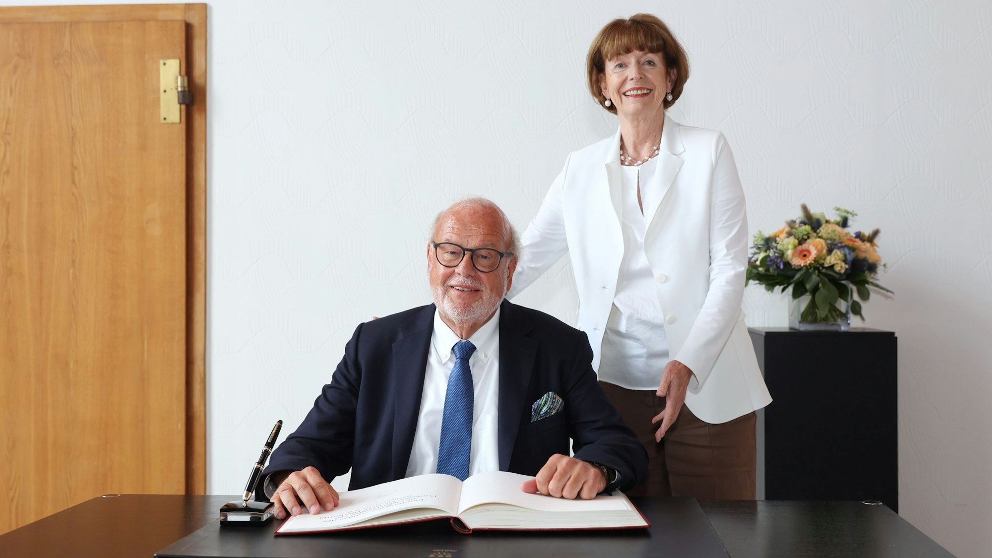 Oberbürgermeisterin Henriette Reker steht neben Prof. Dr. Rolf Bietmann, der an einem Tisch vor einem Buch sitzt