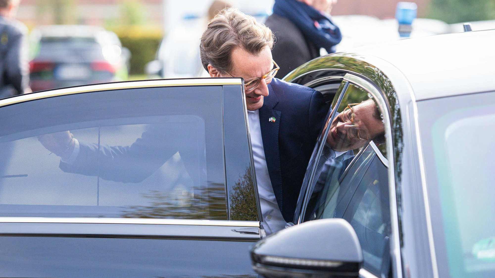 Hendrik Wüst steigt in seinen Dienstwagen ein. Sein Bild spiegelt sich.