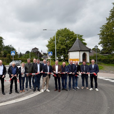 Mehrere Menschen stehen auf der neu hergerichteten Straße und zerschneiden ein rot-weißes Band.