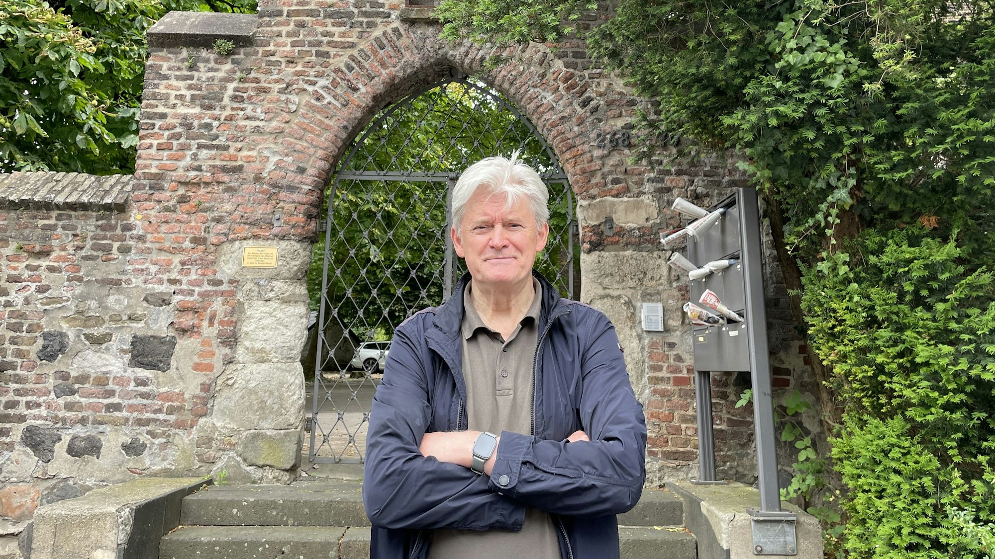 Wilhelm Jüllich steht vor dem Eingangstor der alten Pfarrkirche Alt. St. Pankratius in Köln-Worringen.