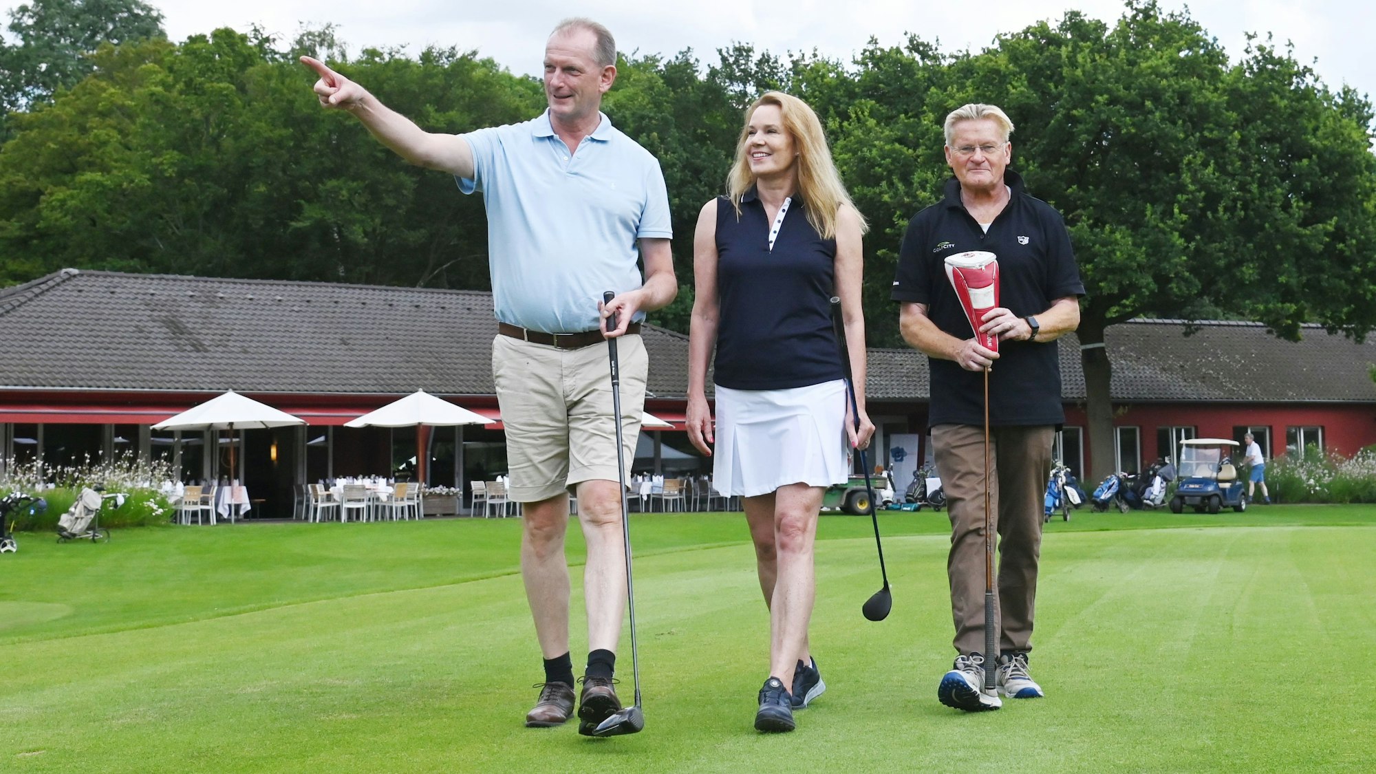 Das Bild zeigt drei Personen, die über den Rasen eines Golfplatzes gehen.