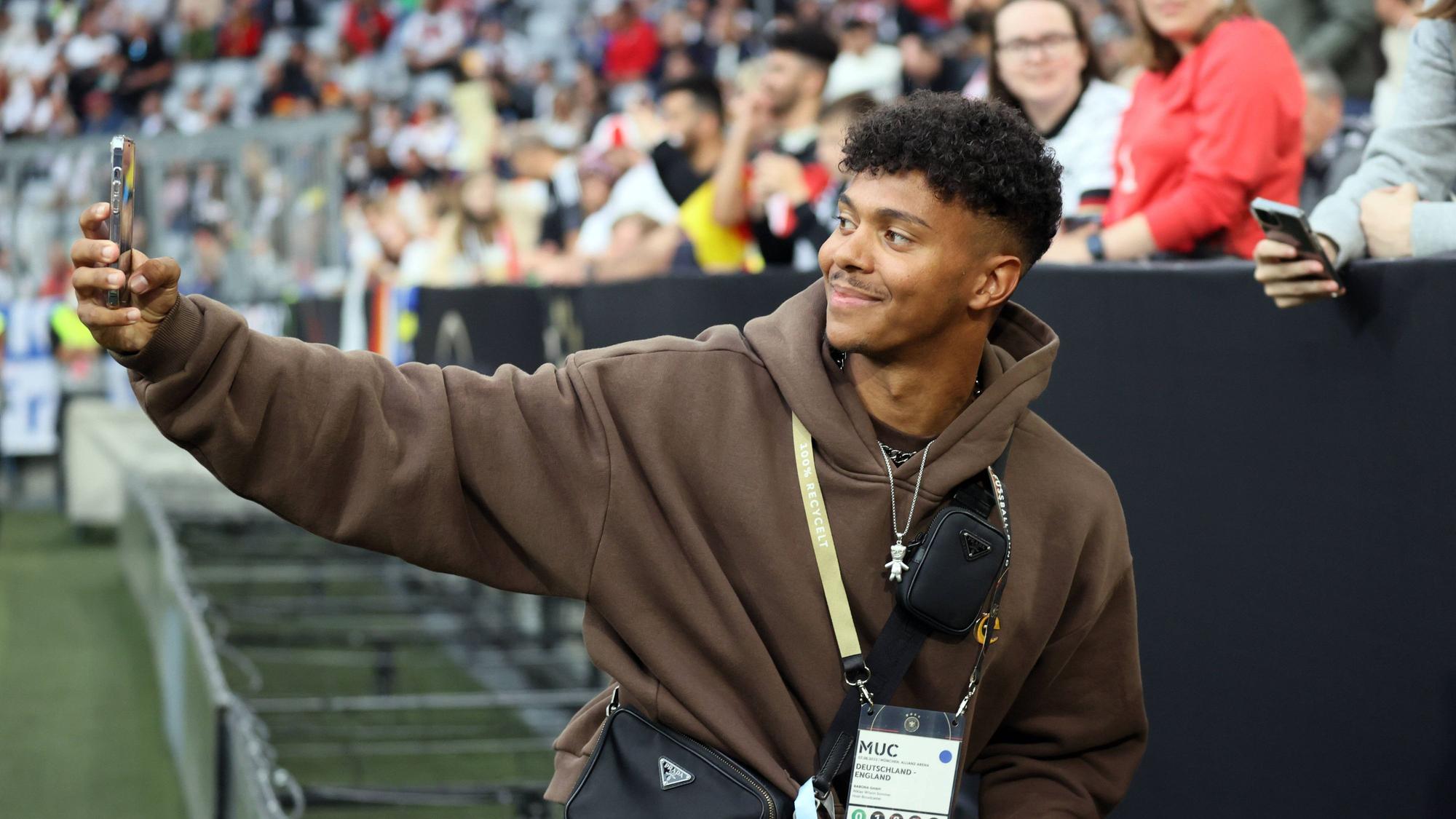 Ein Mann steht im Innenraum eines Fußballstadions und filmt sich selbst mit dem Smartphone.