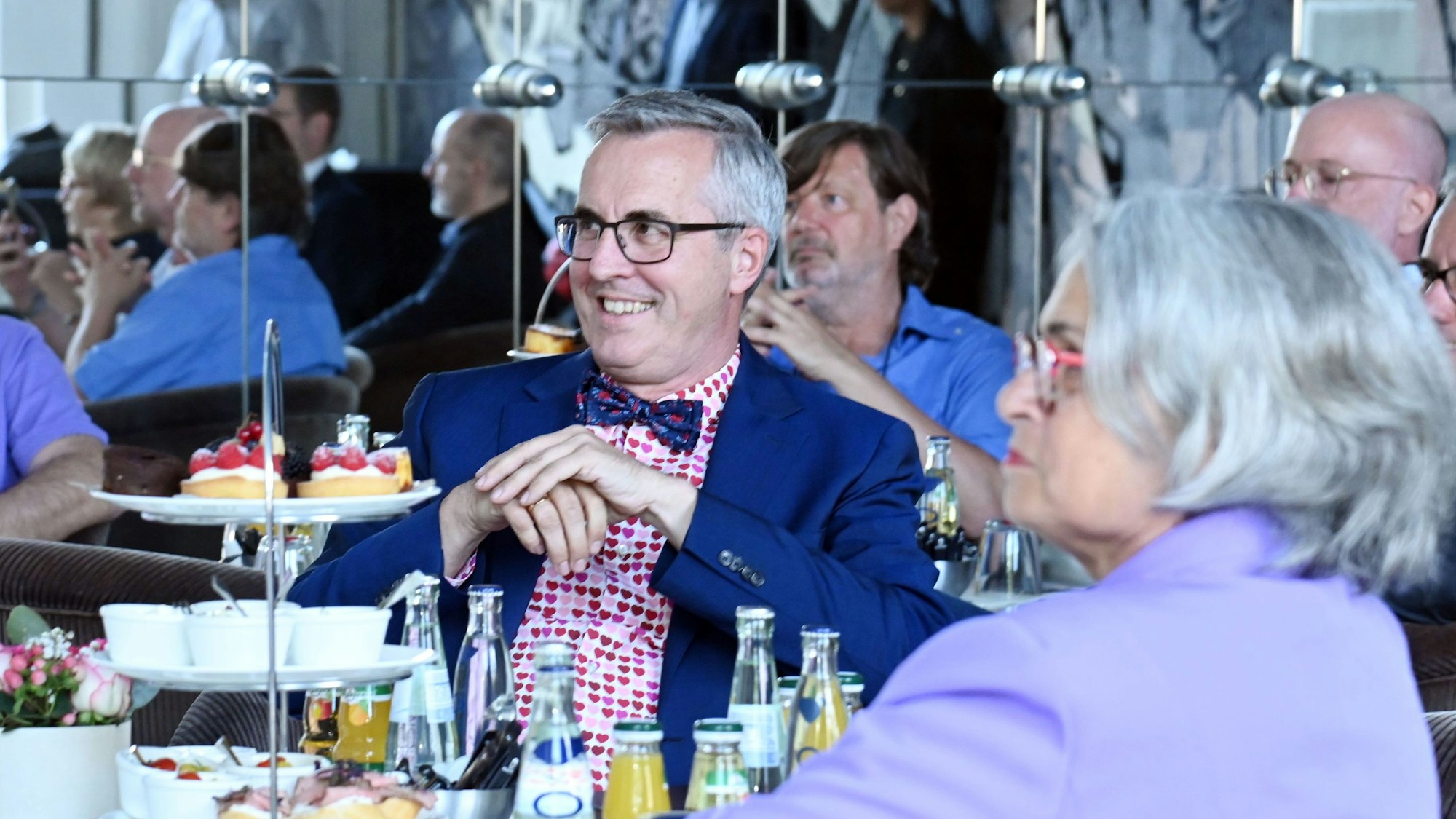 Zu sehen sind mehrere Menschen, die vor gedeckten Tischen sitzen. Im Vordergrund sitzt Andreas Wolter.