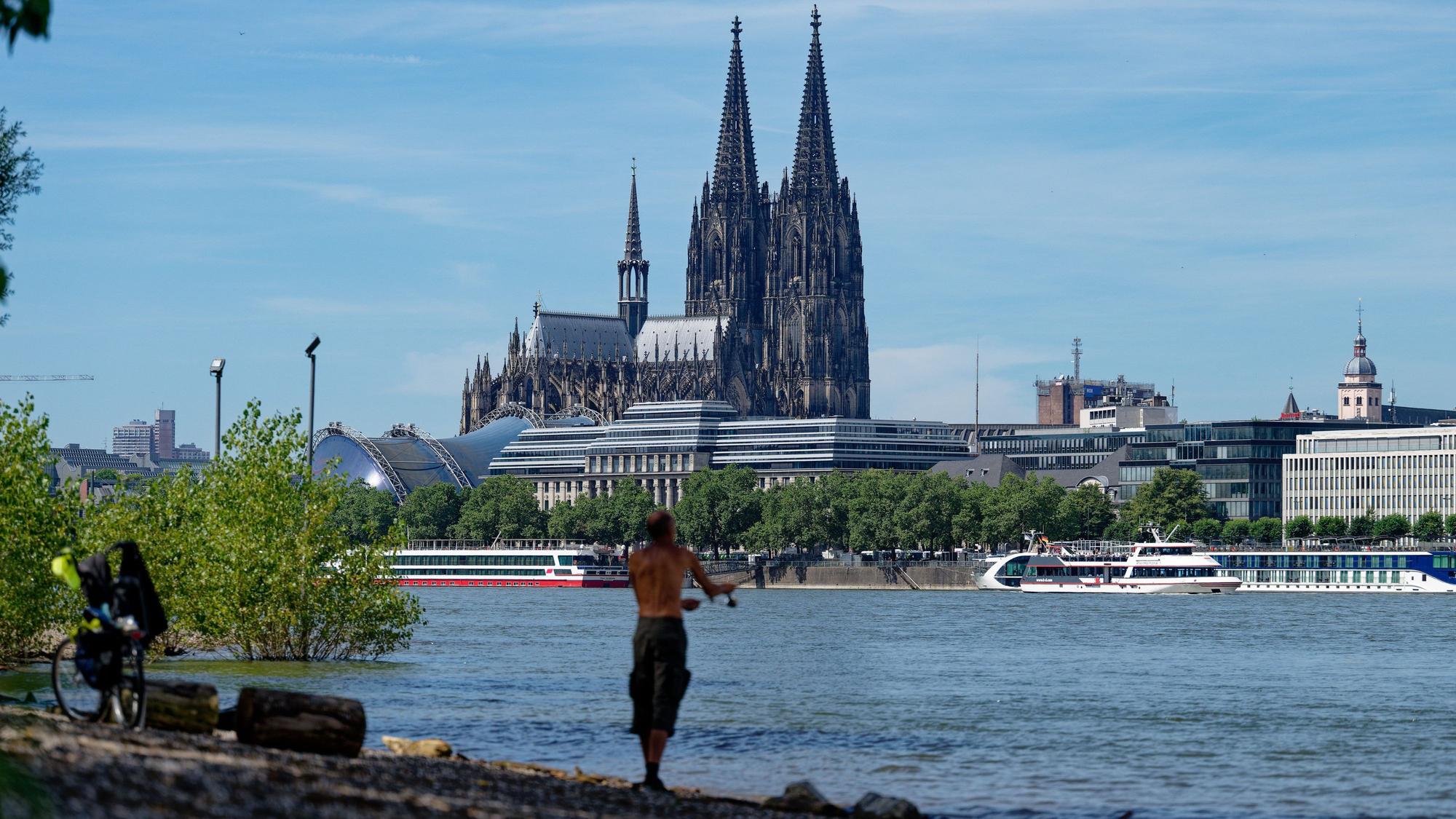09.07.2024, Nordrhein-Westfalen, Köln: Ein Angler steht bei Hochsommerwetter am Rhein und angelt. Im Hintergrund ist der Dom zu sehen. Foto: Henning Kaiser/dpa +++ dpa-Bildfunk +++