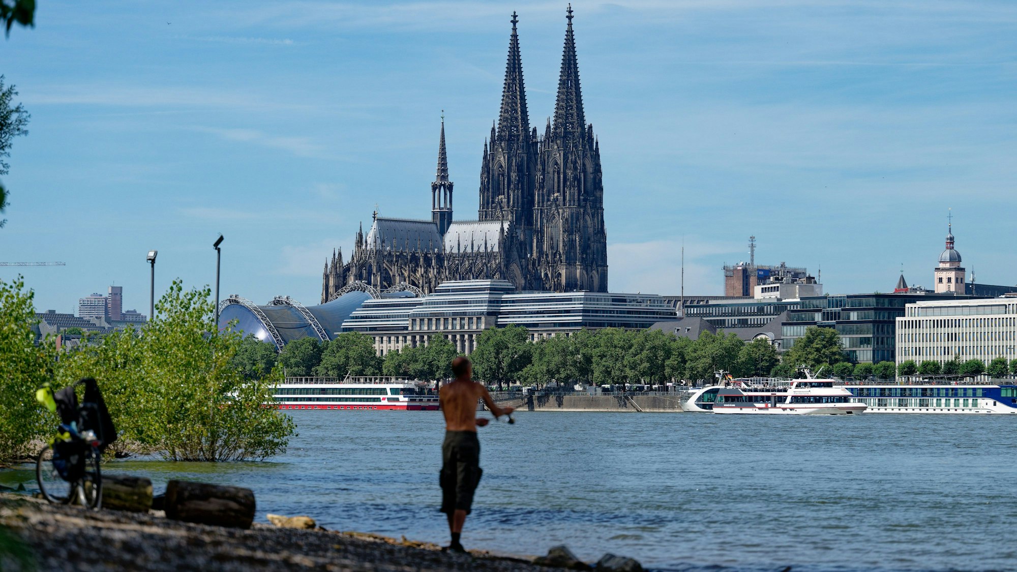 09.07.2024, Nordrhein-Westfalen, Köln: Ein Angler steht bei Hochsommerwetter am Rhein und angelt. Im Hintergrund ist der Dom zu sehen. Foto: Henning Kaiser/dpa +++ dpa-Bildfunk +++