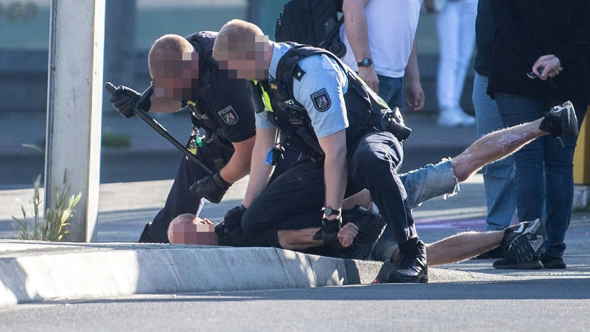 Das Bild zeigt zwei Polizisten, die einen Mann auf den Boden drücken. Der Mann liegt auf dem Bauch.