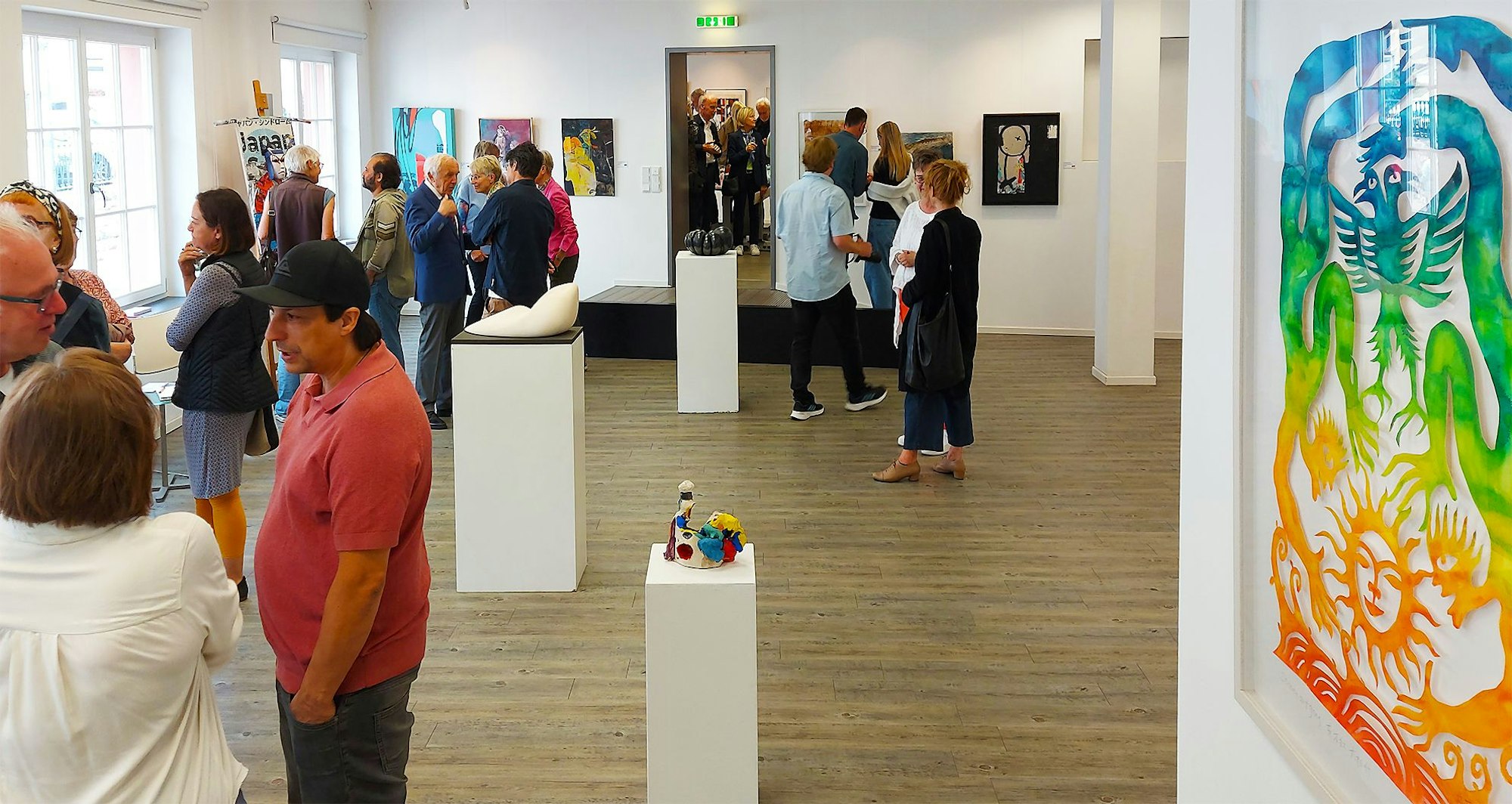 Zahlreiche Menschen stehen in einem Raum und betrachten die Kunstwerke einer Ausstellung.