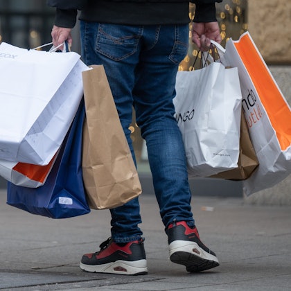 Mit vollen Einkaufstüten in den Händen geht ein Mann über eine Einkaufsstraße.