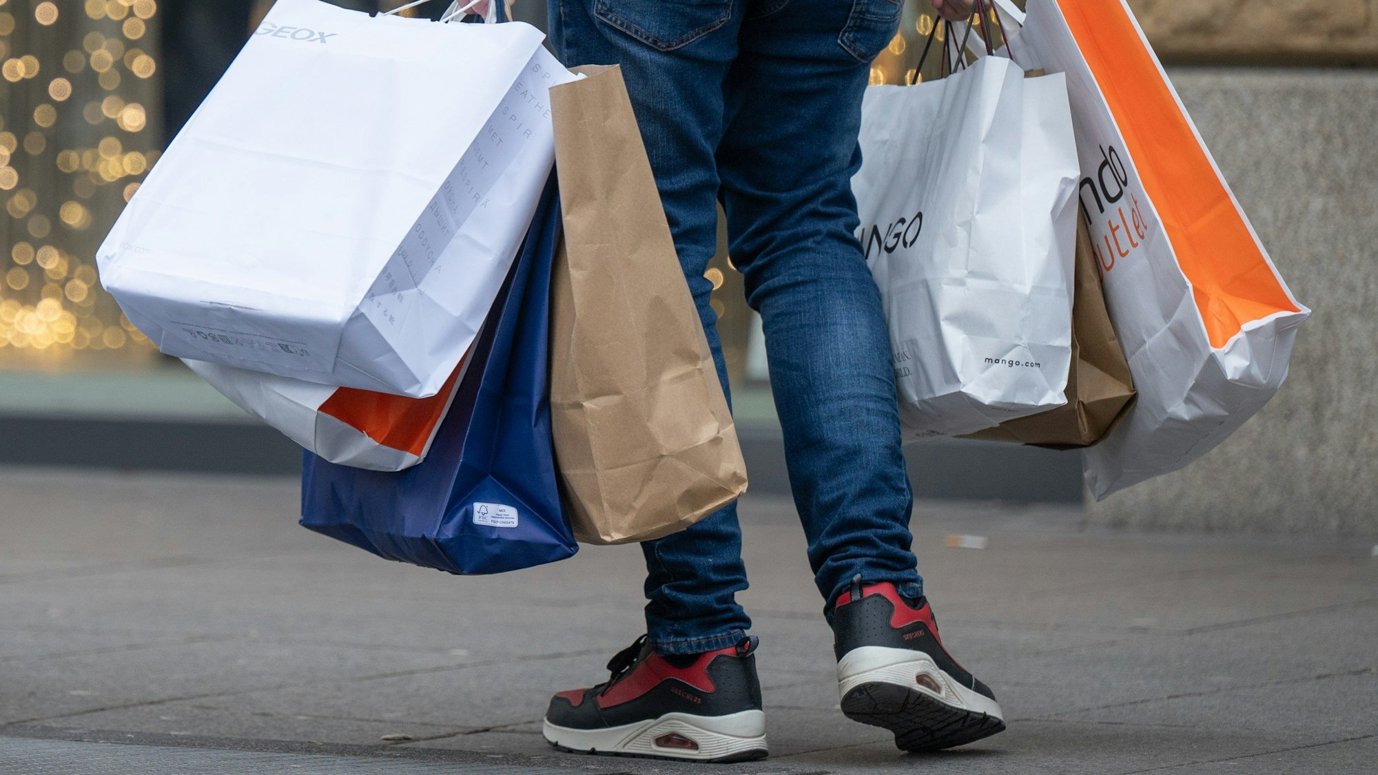 Mit vollen Einkaufstüten in den Händen geht ein Mann über eine Einkaufsstraße.