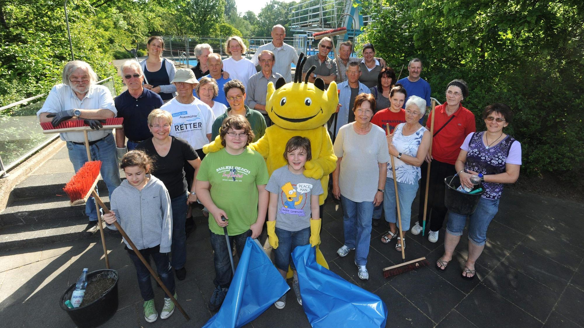 Eine Gruppe Menschen steht am Freibad Auermühle zusammen. In der Hand halten sie Müllsäcke und Besen.