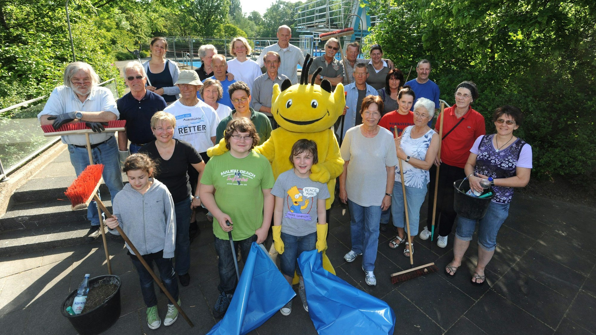 Eine Gruppe Menschen steht am Freibad Auermühle zusammen. In der Hand halten sie Müllsäcke und Besen.