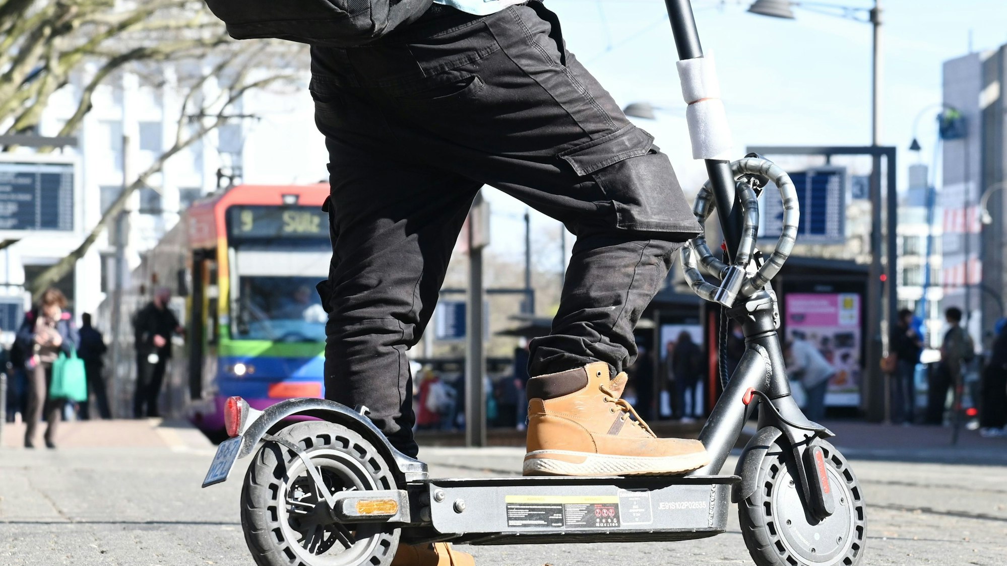 Ein E-Scooter Fahrer vor einer KVB Bahn am Neumarkt.