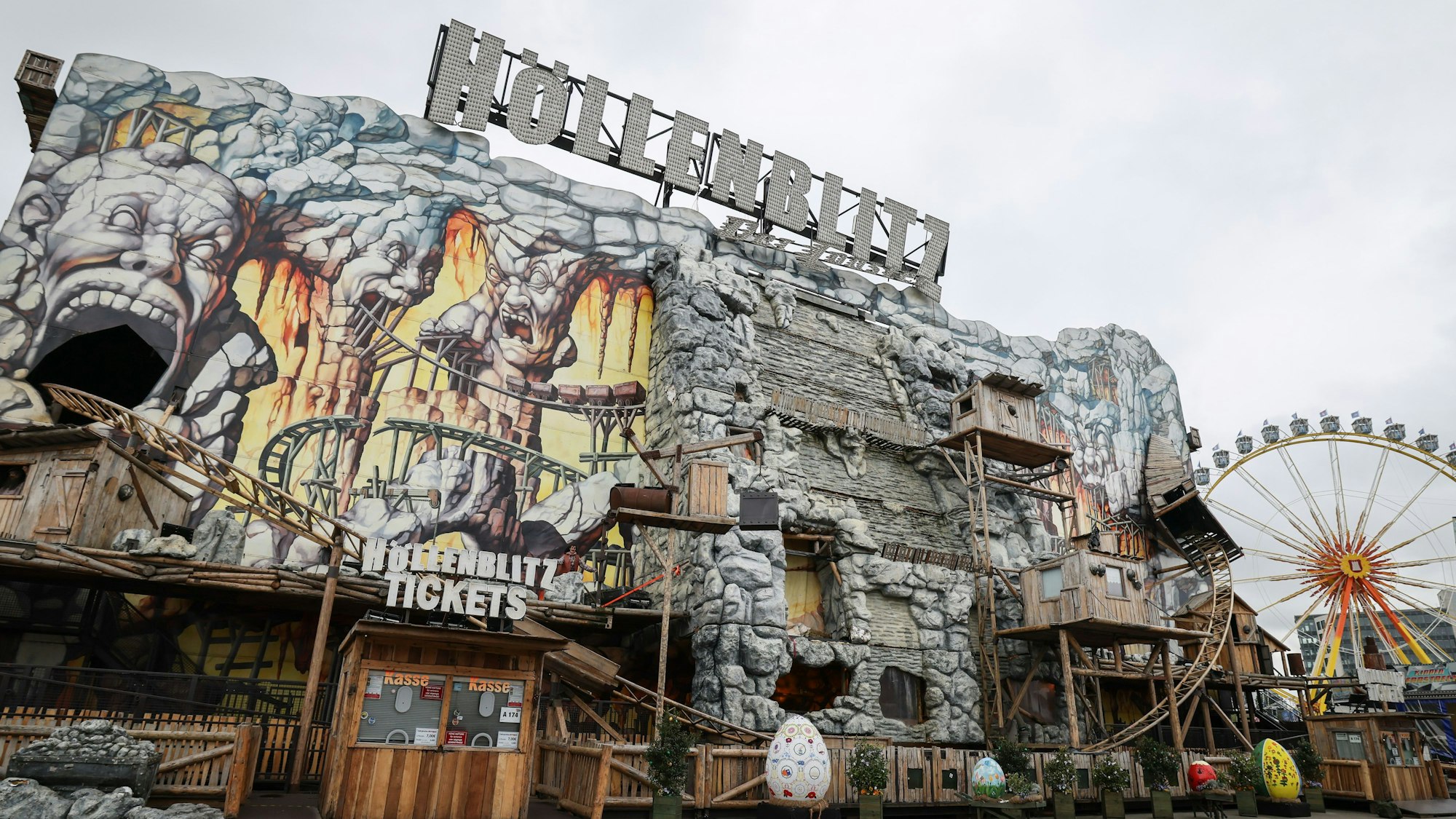 Die Achterbahn „Höllenblitz“ auf dem Hamburger Dom. Zu sehen sind Teile der Schienen, die außen an der Anlage entlangführen. Die Anlage sieht aus wie aus Stein gehauen und imitiert eine Mine.