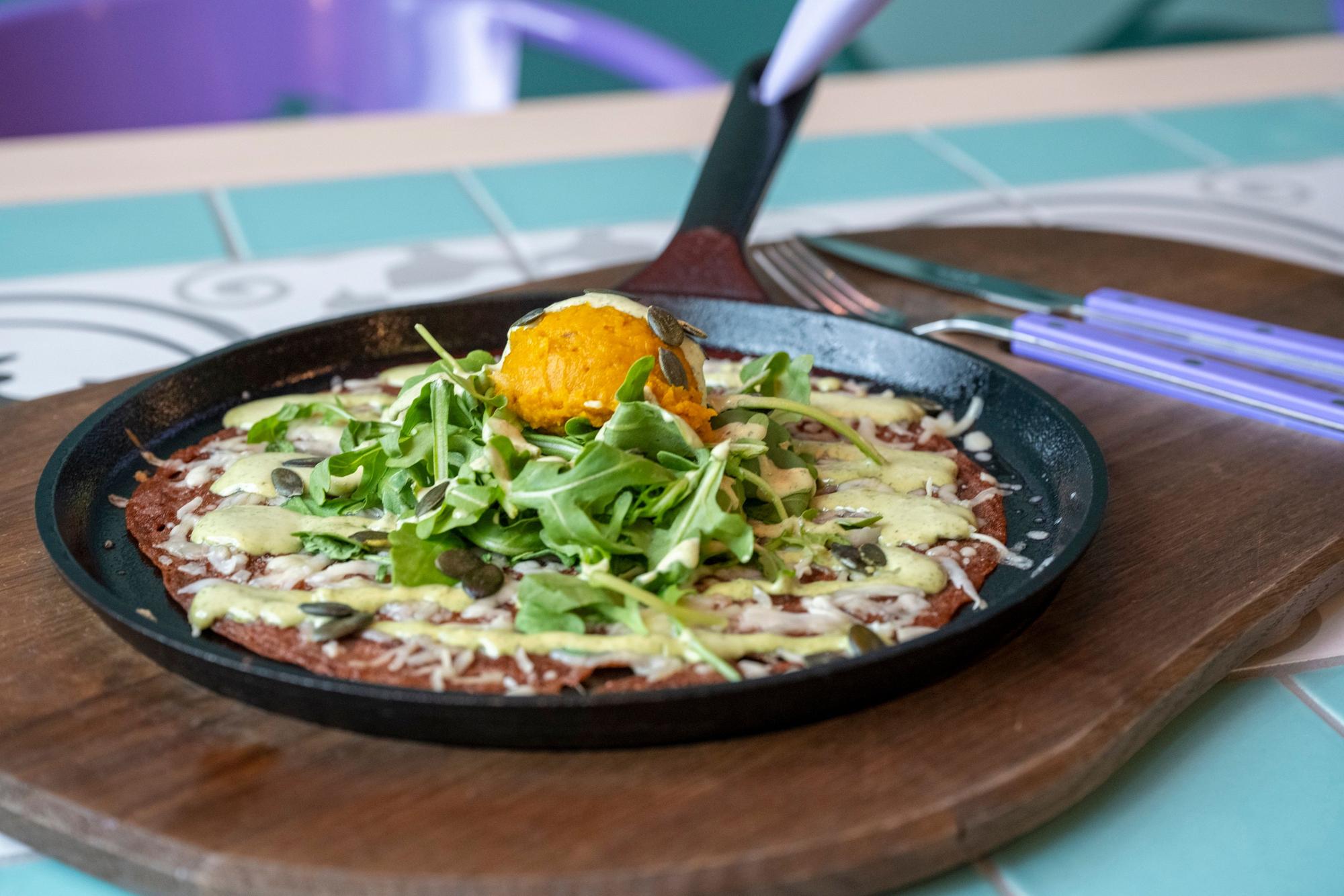 Eine Galette Roussillon (herzhafter Crêpe) mit Kürbispüree, verschiedenem Käse, Rucola und Salbei-Sauce in einer Servierpfanne angerichtet.