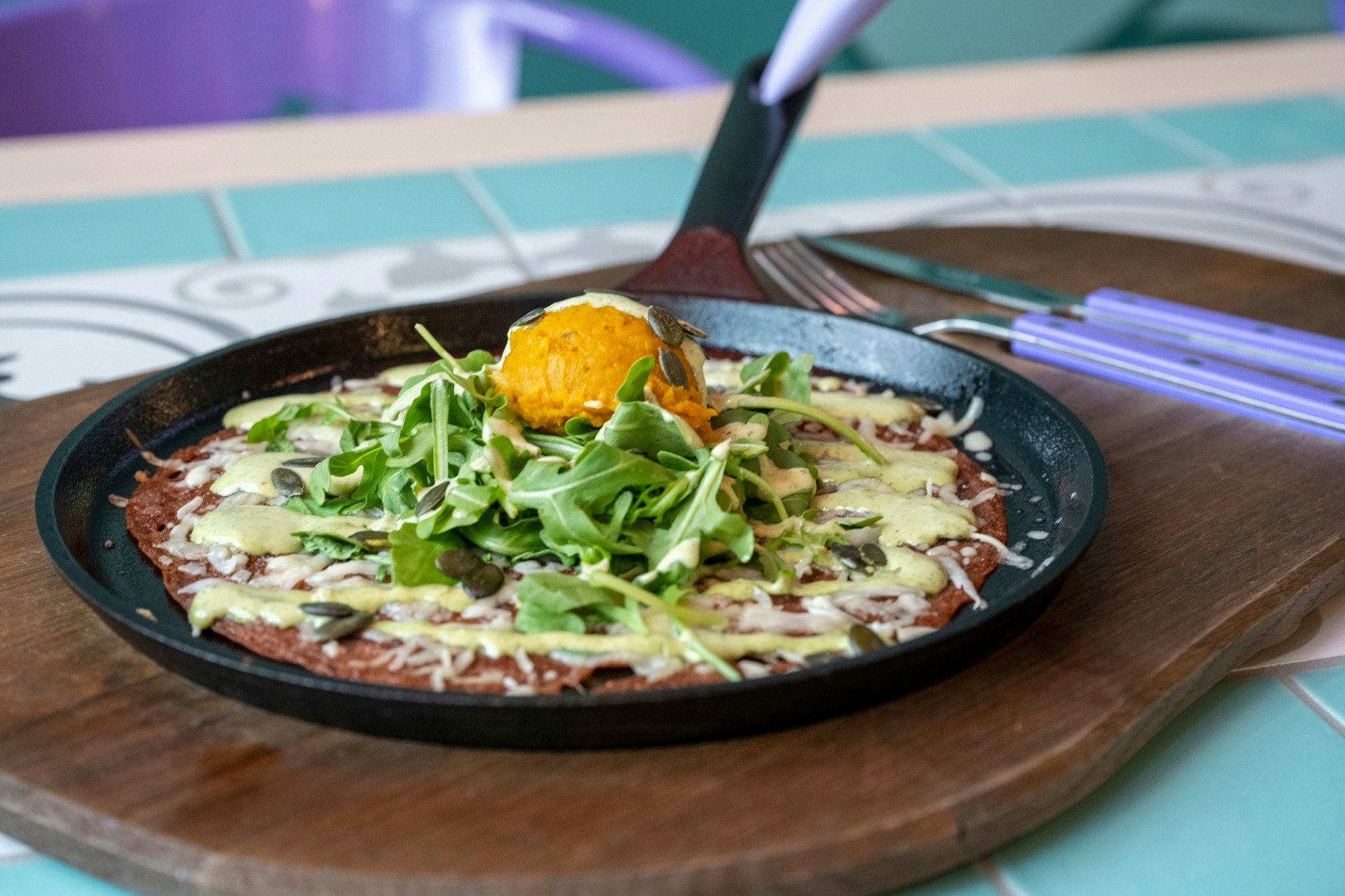 Eine Galette Roussillon (herzhafter Crêpe) mit Kürbispüree, verschiedenem Käse, Rucola und Salbei-Sauce in einer Servierpfanne angerichtet.