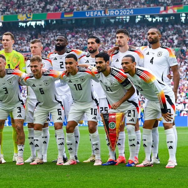 Die deutsche Nationalmannschaft posiert in zwei Reihen auf dem Spielfeld: Manuel Neuer, Toni Kroos, Antonio Rüdiger, Emre Can, Kai Havertz, Jonathan Tah, David Raum, Joshua Kimmich, Jamal Musiala, Ilkay Gündogan und Leroy Sané. Im Hintergrund sind voll besetzte Stadionränge zu sehen.