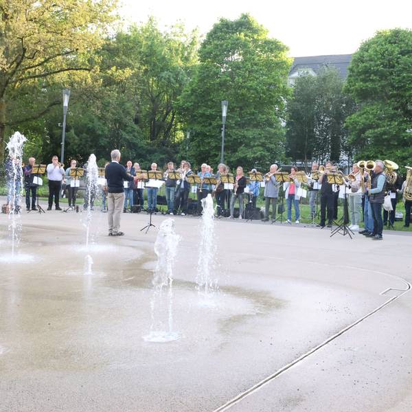 Ein Blasorchester spielt, im Vordergrund sieht man ein Wasserspiel.