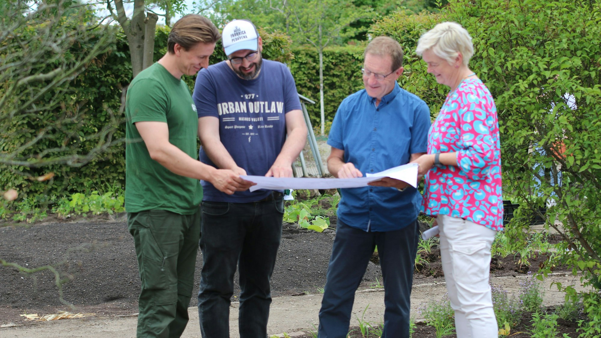 Gartenbauer Lukas Werker, Architekt Sven Berkey, Fachbereichsleiter Stadtgrün Uli Hammer und Abteilungsleiterin Silke Thyssen stehen nebeneinander im Garten und gucken auf einen Plan.
