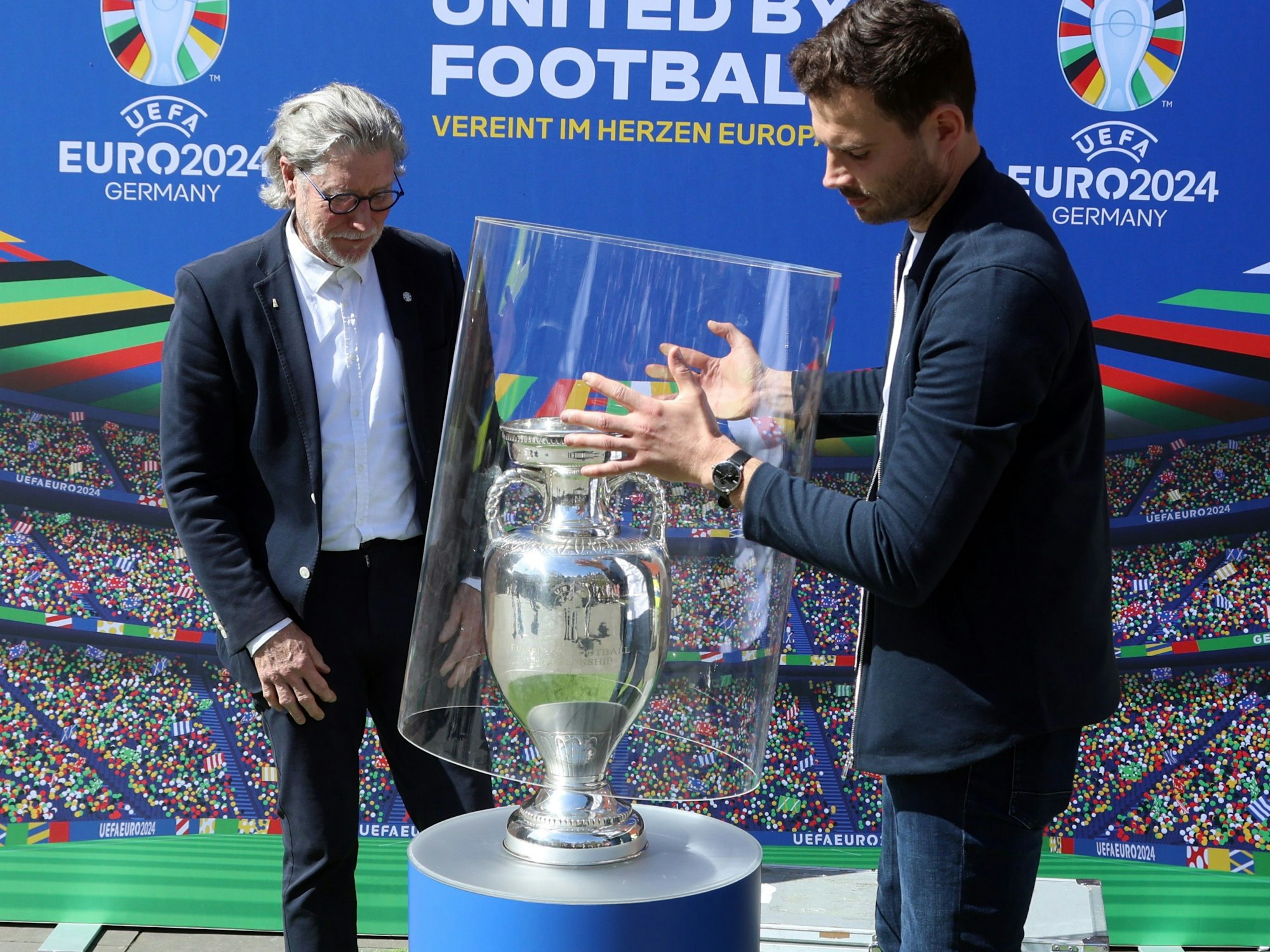 Das Bild zeigt Stefan Kühlborn, wie er für Toni Schumacher die Schutzglocke vom EM-Pokal entfernt.