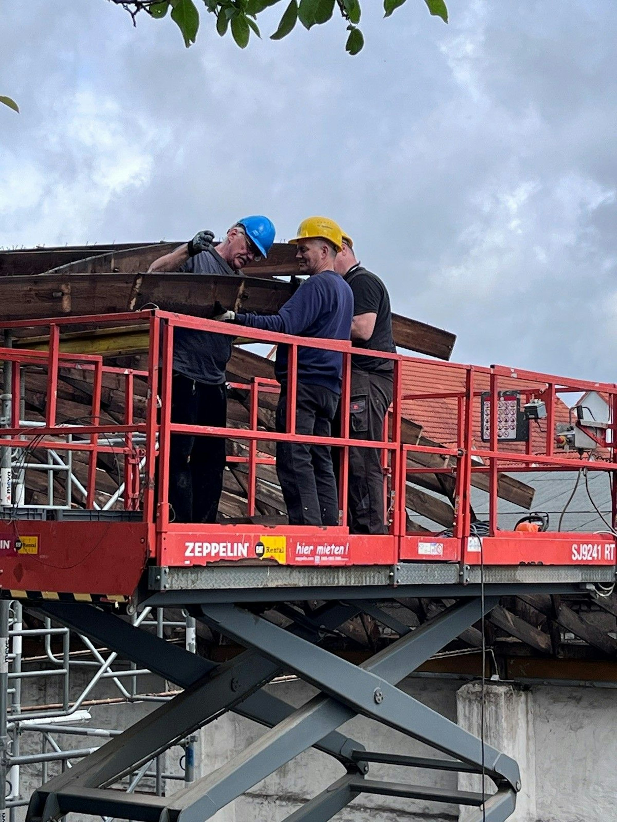 Drei Männer mit Bauhelmen stehen auf einer Hebebühne.