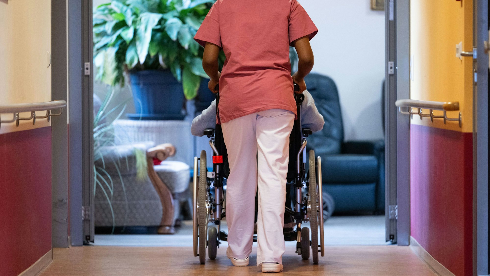 Eine Bewohnerin eines Pflegeheims wird von einer Pflegerin einen Gang entlang geschoben.