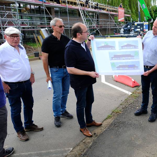 Mehrere Personen blicken auf einen Bauplan der Bürgerhalle Kall, der von Hermann-Josef Esser (3.v.r.) und Stefan Kupp (3.v.l.) gehalten wird.