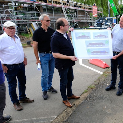 Mehrere Personen blicken auf einen Bauplan der Bürgerhalle Kall, der von Hermann-Josef Esser (3.v.r.) und Stefan Kupp (3.v.l.) gehalten wird.