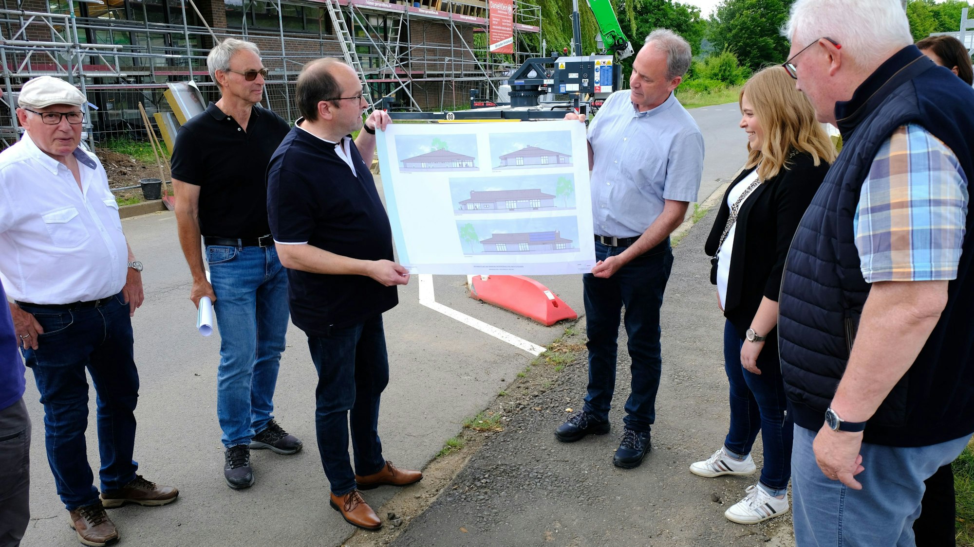 Mehrere Personen blicken auf einen Bauplan der Bürgerhalle Kall, der von Hermann-Josef Esser (3.v.r.) und Stefan Kupp (3.v.l.) gehalten wird.