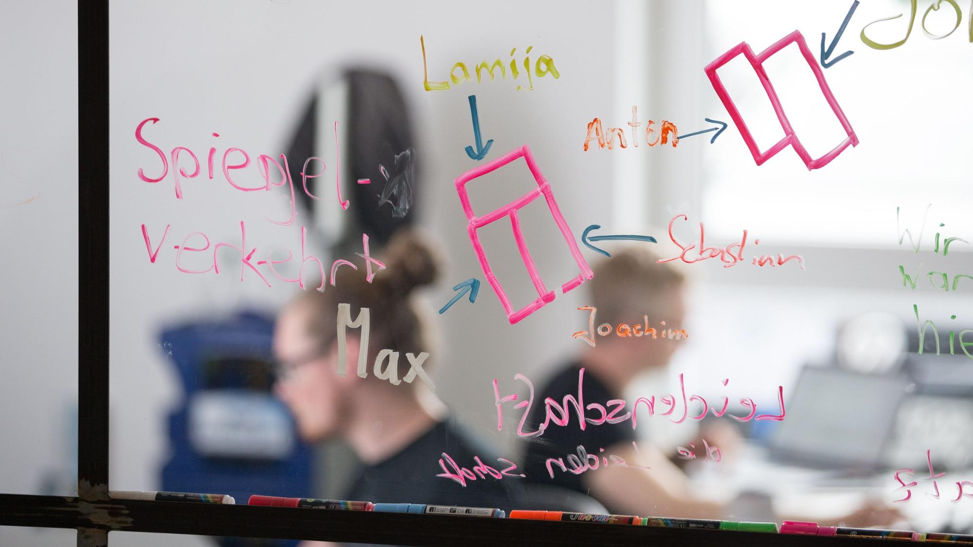 Mitarbeiter einer Start-up-Firma sitzen hinter einer Scheibe.
