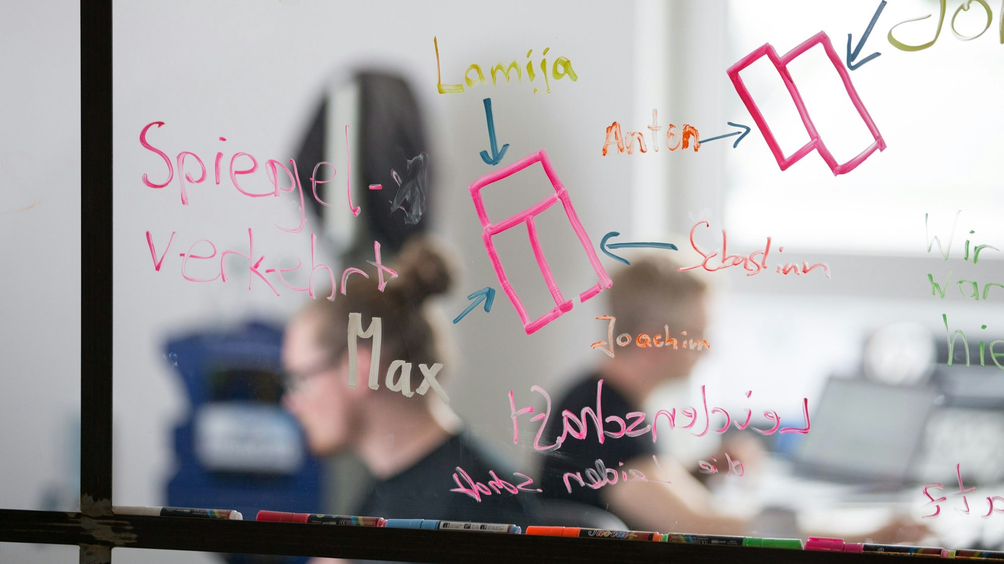 Mitarbeiter einer Start-up-Firma sitzen hinter einer Scheibe.