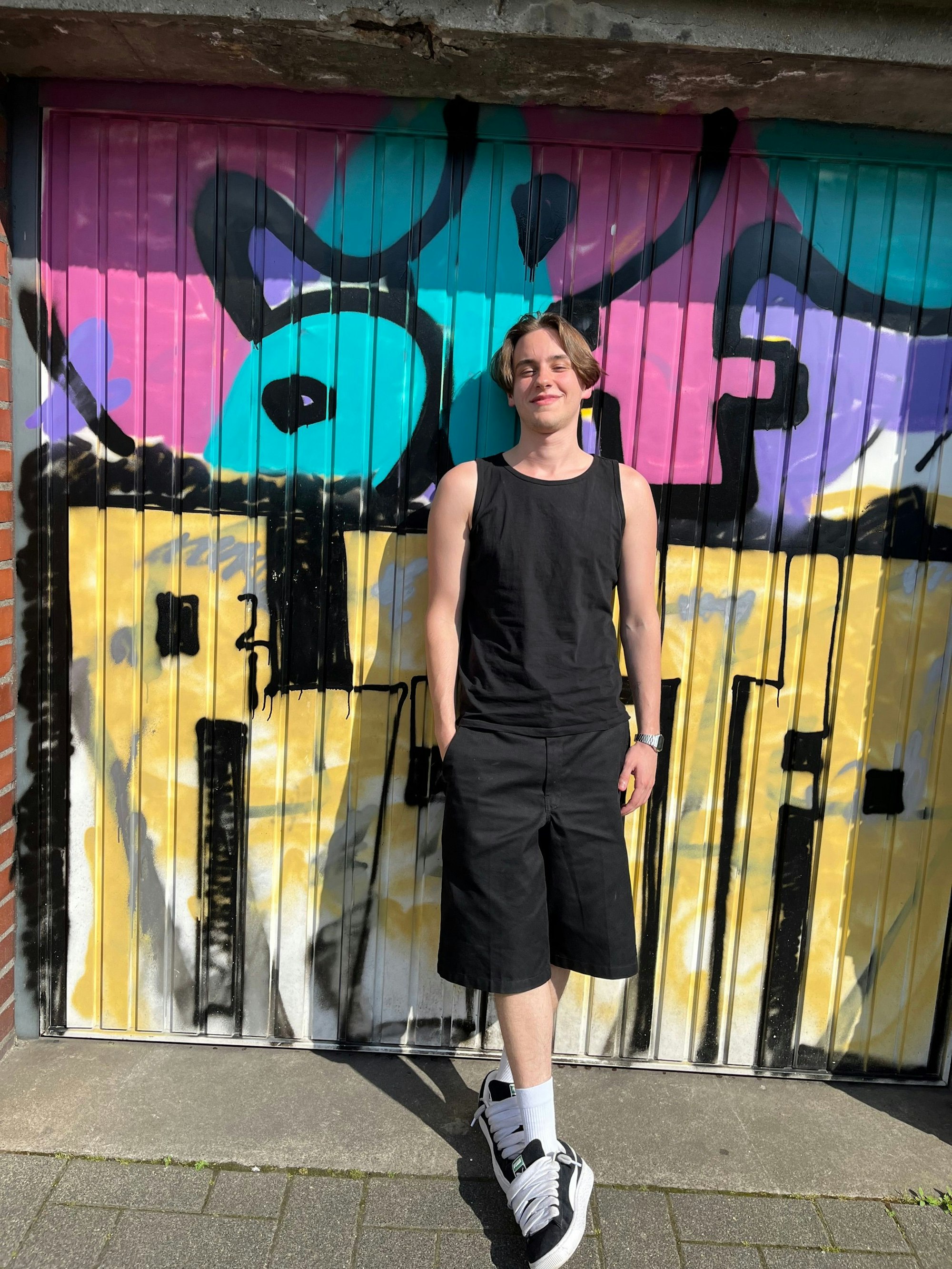 Porträt von Tristan Simon, der an einer mit Graffiti besprühten Garage lehnt.