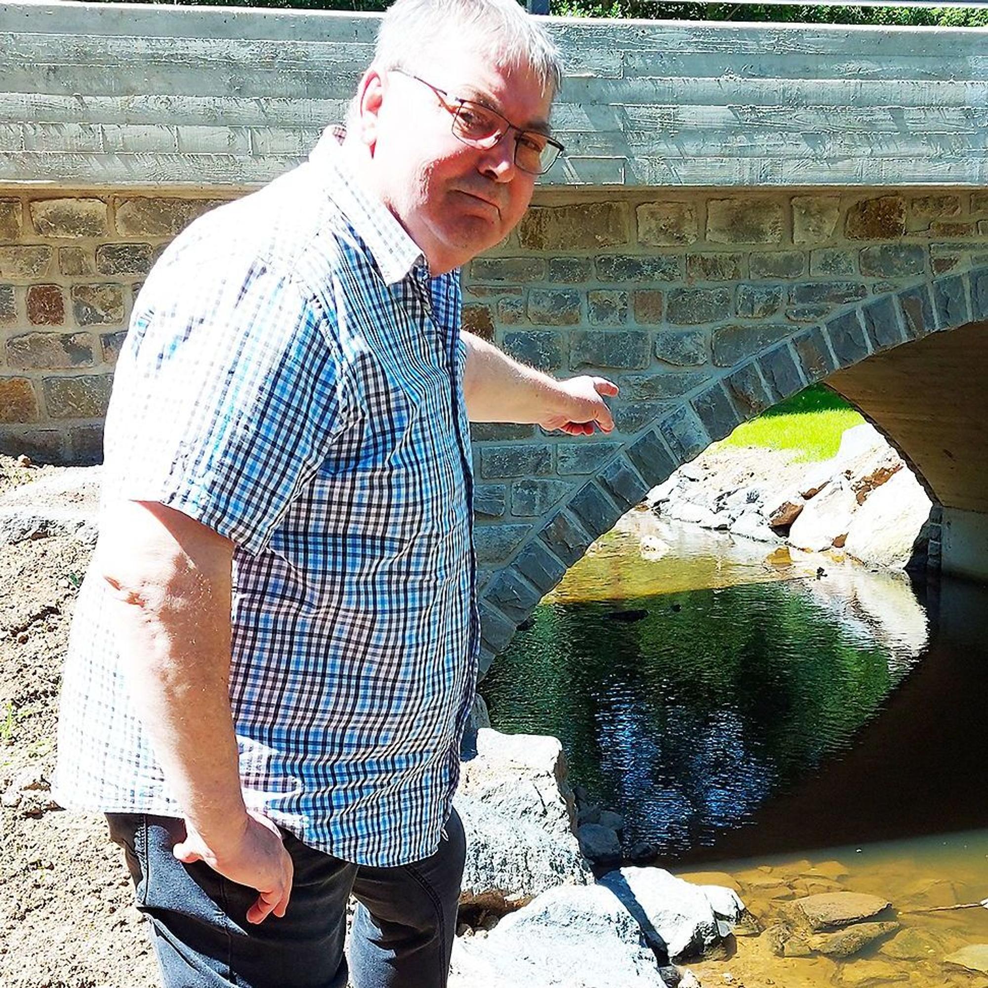 Martin Peetz steht am Rande des Flusses und zeigt auf die Brücke.