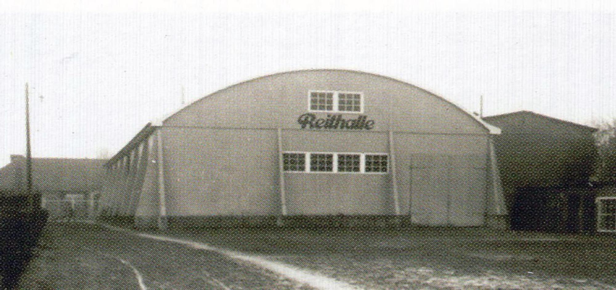 Ein schwarz-weiß Bild zeigt eine Halle mit Walmdach und der Aufschrift Reithalle.