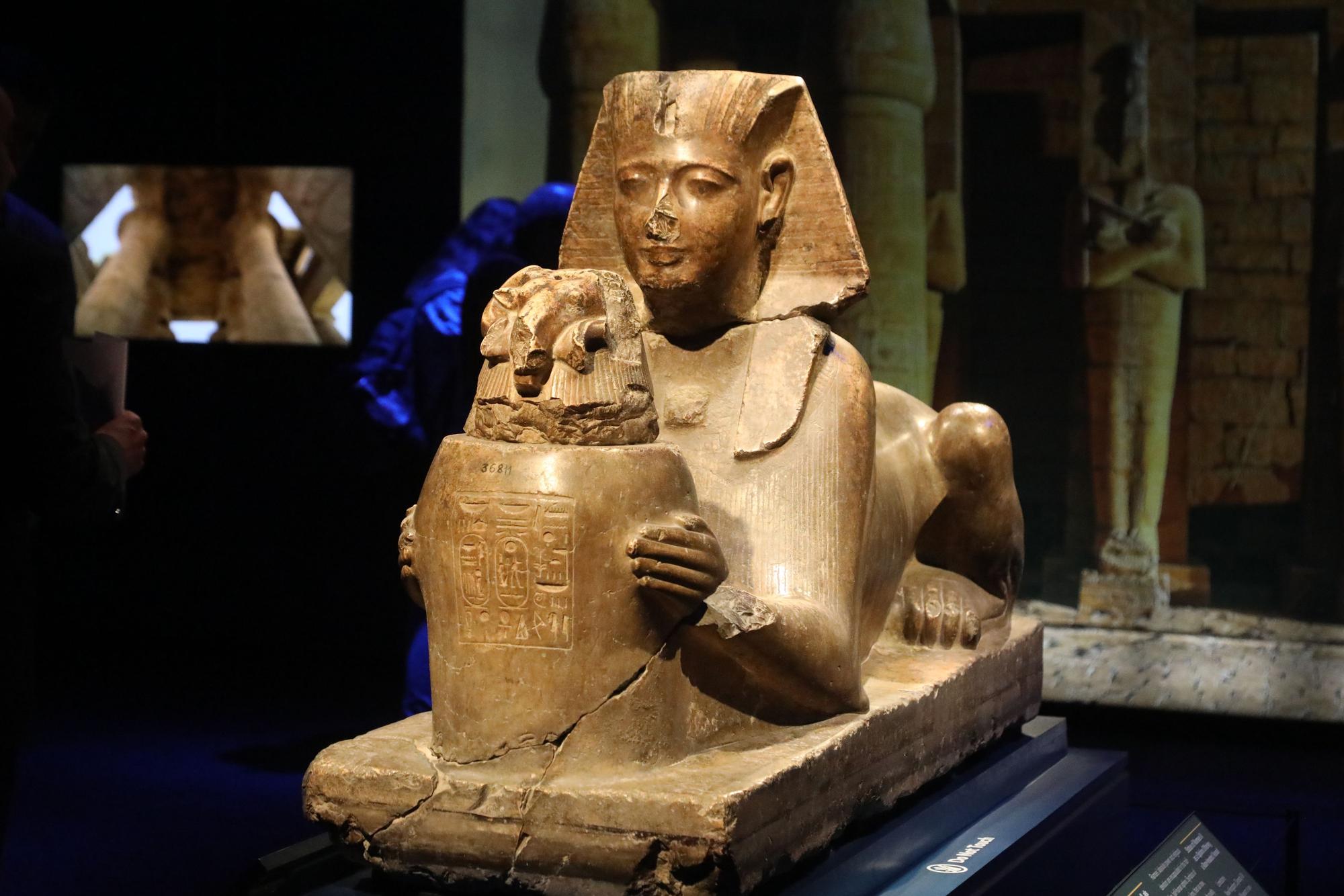 Eine liegende Sphinx hält eine Vase in den Händen.