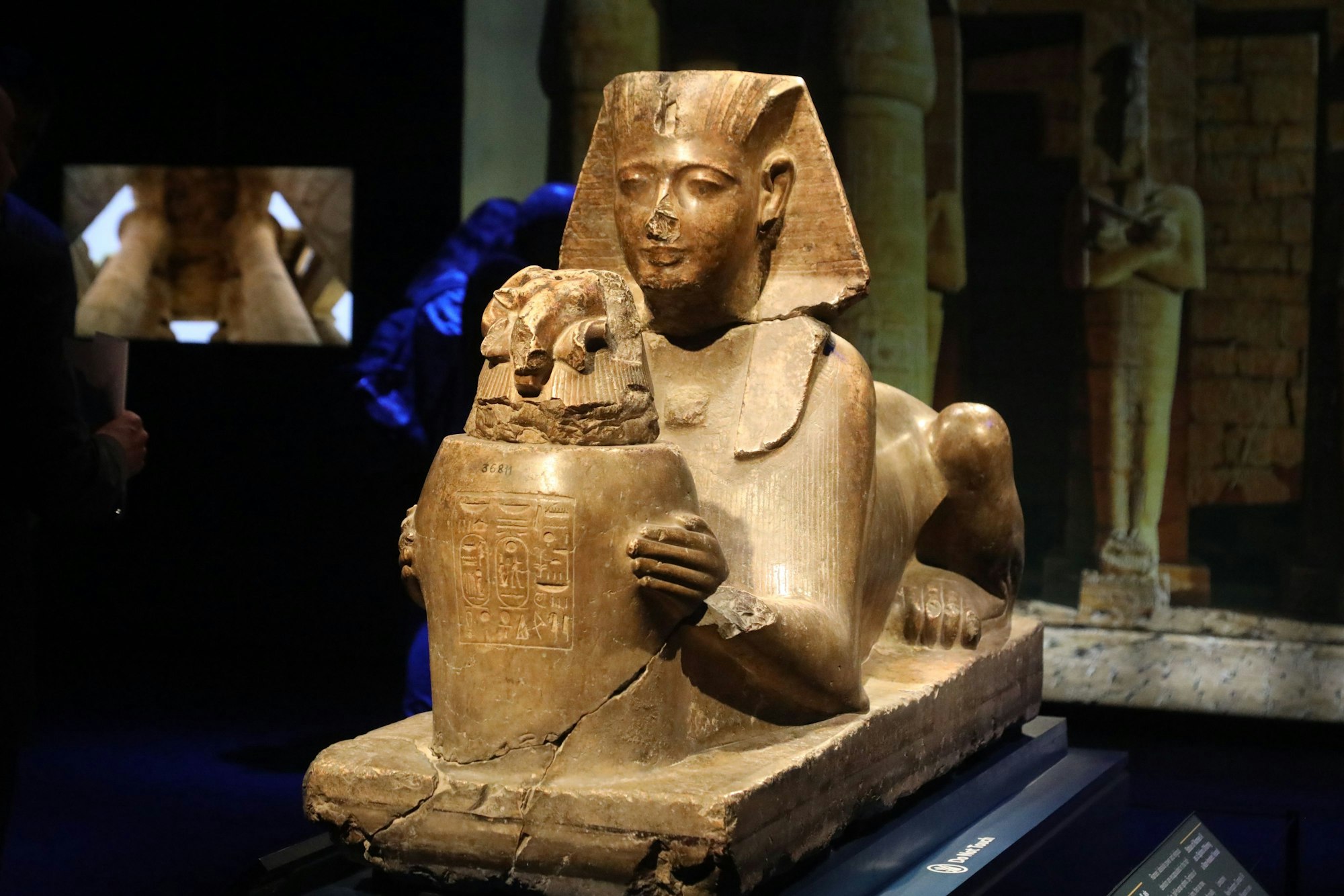 Eine liegende Sphinx hält eine Vase in den Händen.