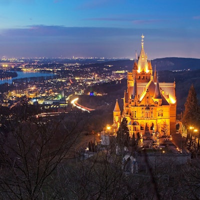 Beleuchtetes Schloss Drachenburg über dem Rheintal am Abend.